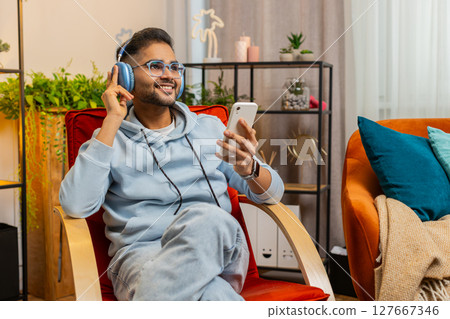 Happy relaxed man in wireless headphones dancing listening favorite disco pop music on home chair 127667346
