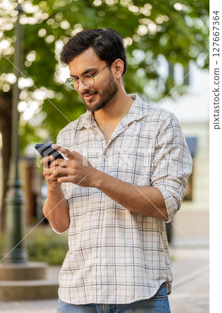 Indian young man using smartphone typing text messages in social media application online on street 127667364