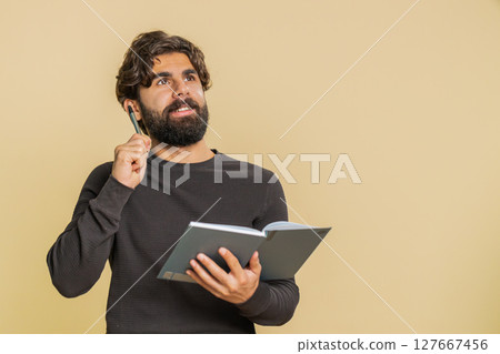 Thoughtful businessman making notes, writing down thoughts with pen into diary on beige background 127667456