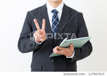 A middle-aged male businessman in a suit holding a binder and making a peace sign 127667614