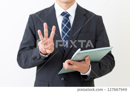 A middle-aged male businessman in a suit holding a binder and pointing three fingers up A middle-aged male businessman in a suit holding a binder and pointing three fingers up 127667949