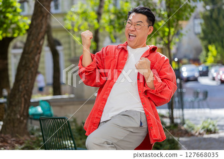 Asian man shouting celebrating success winning goal achievement good victory news on city street Asian man shouting celebrating success winning goal achievement good victory news on city street 127668035