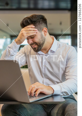 Tired ill young businessman using laptop suffering from headache problem tension in hotel lobby Tired ill young businessman using laptop suffering from headache problem tension in hotel lobby 127668206