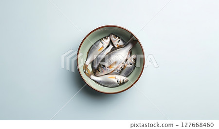 Fish are artistically arranged in a ceramic bowl with muted earthy tones, their scales glisten under soft lighting. The composition emphasizes simplicity and minimalism Fish are artistically arranged in a ceramic bowl with muted earthy tones, their scales glisten under soft lighting. The composition emphasizes simplicity and minimalism 127668460