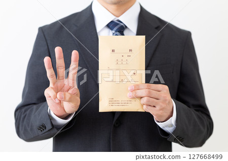 A middle-aged male businessman in a suit holding a pay envelope and raising three fingers 127668499