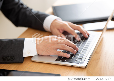 A middle-aged male businessman in a suit working on a computer at a desk A middle-aged male businessman in a suit working on a computer at a desk 127669772