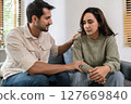 Supportive couple in emotional moment at home as woman struggles with sadness and stress, expressing 127669840