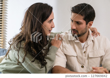 Supportive couple in emotional moment at home as woman struggles with sadness and stress, expressing 127669842
