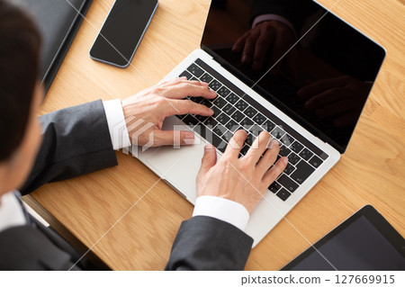 A middle-aged male businessman in a suit working on a computer at a desk A middle-aged male businessman in a suit working on a computer at a desk 127669915