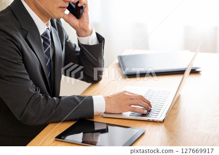 A middle-aged male businessman in a suit working on a computer at a desk 127669917