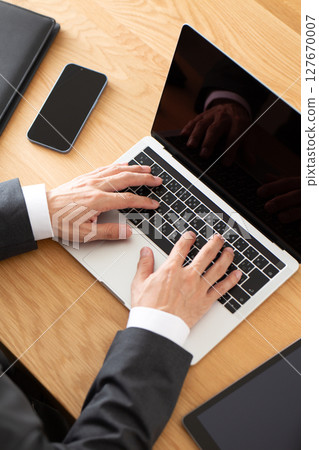 A middle-aged male businessman in a suit working on a computer at a desk 127670007