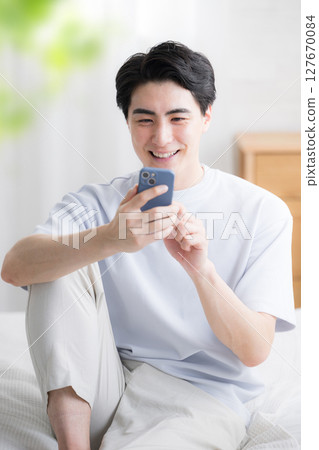 Full body of a refreshing man relaxing in bed and holding a smartphone 127670084
