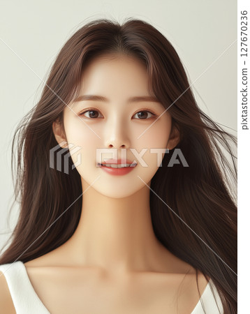 Young Korean woman with long hair smiling softly in a light-colored studio setting 127670236