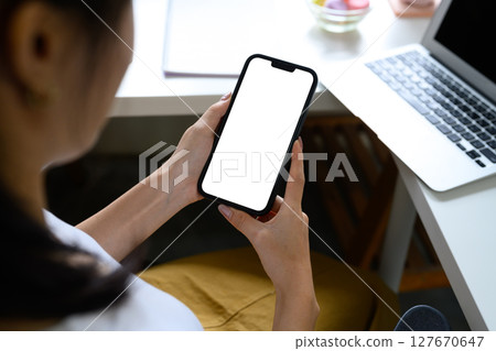 Close up of woman holding smartphone with blank white screen at modern workspace. Close up of woman holding smartphone with blank white screen at modern workspace. 127670647