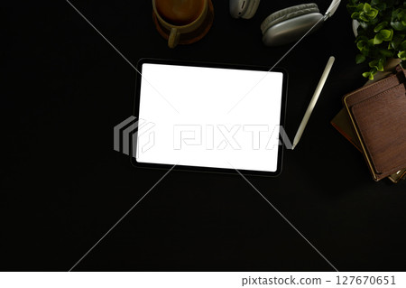 Flat lay of digital tablet with blank screen on dark workspace desk with coffee and headphones Flat lay of digital tablet with blank screen on dark workspace desk with coffee and headphones 127670651