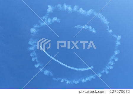 A smiley face painted in the blue sky by aerobatic flight 127670673