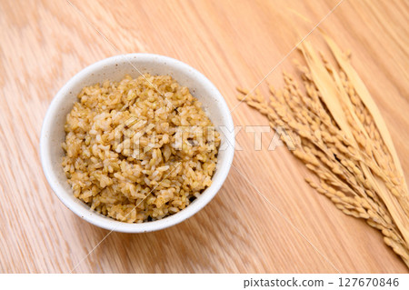 Brown rice and ears of rice in a bowl on a wooden table background Brown rice and ears of rice in a bowl on a wooden table background 127670846