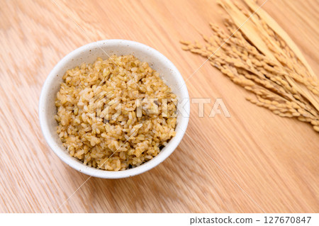 Brown rice and ears of rice in a bowl on a wooden table background Brown rice and ears of rice in a bowl on a wooden table background 127670847