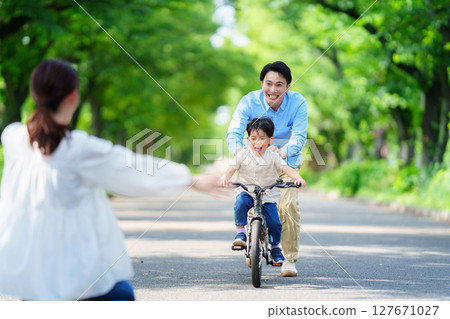 : 5-year-old boy practicing riding a bike with his parents : 5-year-old boy practicing riding a bike with his parents 127671027