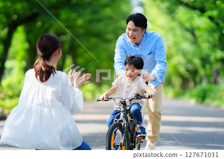 : 5-year-old boy practicing riding a bike with his parents 127671031