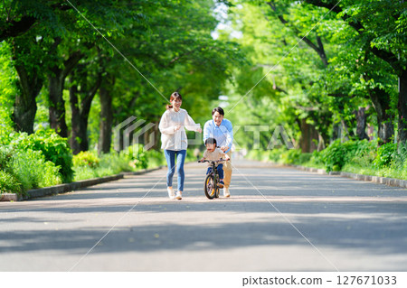 : 5-year-old boy practicing riding a bike with his parents 127671033