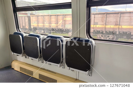 seats in train carriage with view freight cars outside near countryside on clear day. closeup. 127671048