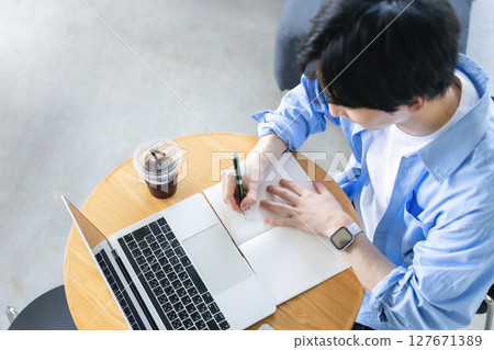 A man taking notes while looking at a computer 127671389