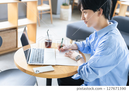 A man taking notes while looking at a computer A man taking notes while looking at a computer 127671390