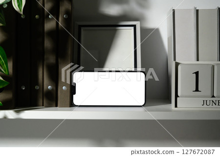 Horizontal mobile phone screen on a shelf, surrounded by books and a calendar block 127672087