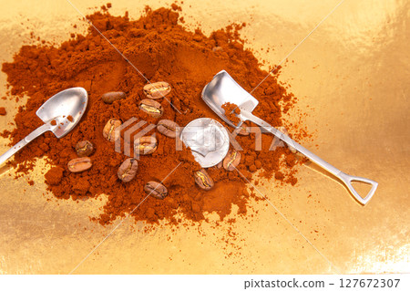 Close-up of two metal shovels in ground coffee, featuring whole beans and a US quarter  127672307