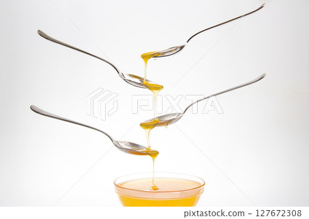 Fresh flower honey drips from a spoon into a spoon on a white background. Organic vitamin food. 127672308