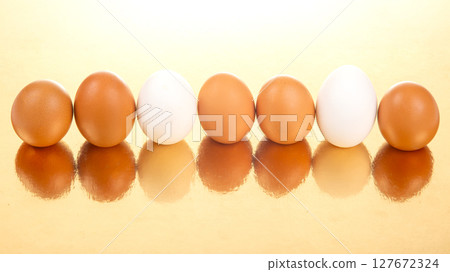 White and brown eggs lined up on a shiny golden background 127672324