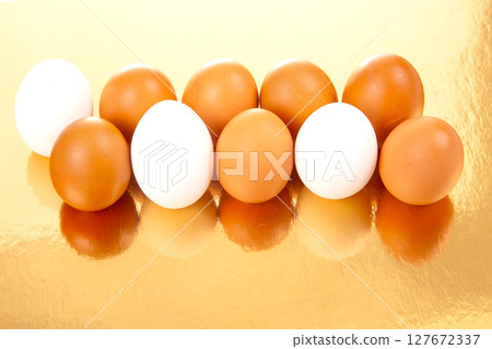 Seven eggs, both white and brown, placed in a row on a reflective golden surface Seven eggs, both white and brown, placed in a row on a reflective golden surface 127672337