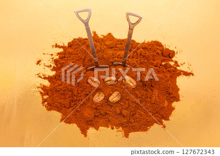two shovels in a pile of rich ground coffee, surrounded by whole coffee beans on a gold background two shovels in a pile of rich ground coffee, surrounded by whole coffee beans on a gold background 127672343