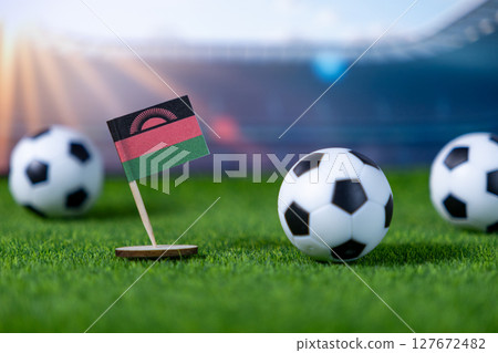 Malawian flag proudly stands with miniature soccer balls on green turf, symbolizing national football team spirit and global sports competition Malawian flag proudly stands with miniature soccer balls on green turf, symbolizing national football team spirit and global sports competition 127672482