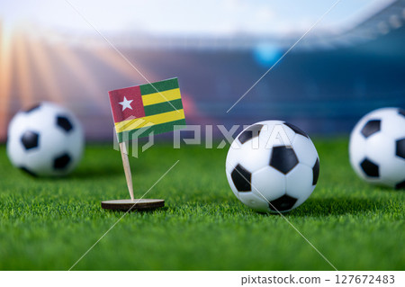 Togo national flag on lush green stadium grass surrounded by soccer balls, representing global football championships, team spirit, and national pride Togo national flag on lush green stadium grass surrounded by soccer balls, representing global football championships, team spirit, and national pride 127672483