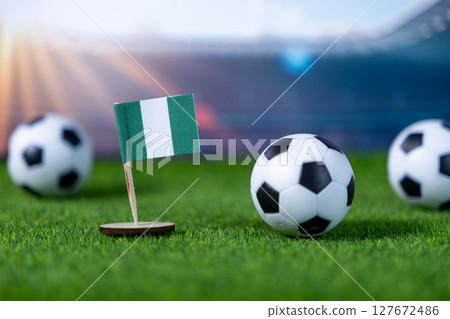 Nigerian flag with small soccer balls on a vibrant green football field representing international sports and national team championship tournaments Nigerian flag with small soccer balls on a vibrant green football field representing international sports and national team championship tournaments 127672486