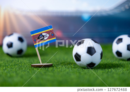 Eswatini flag stands proudly on a vibrant green football pitch with soccer balls, symbolizing national team participation and international sports competition 127672488