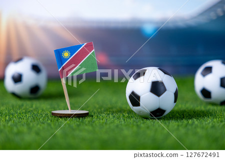 Namibia flag with soccer balls on green grass, set against a blurred stadium backdrop, symbolizing international football competition and national pride Namibia flag with soccer balls on green grass, set against a blurred stadium backdrop, symbolizing international football competition and national pride 127672491