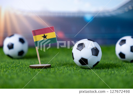 Ghana flag proudly stands on lush green artificial grass with soccer balls, symbolizing national team participation in global sports tournaments Ghana flag proudly stands on lush green artificial grass with soccer balls, symbolizing national team participation in global sports tournaments 127672498
