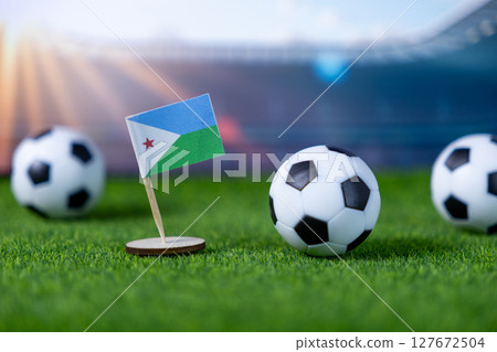 Djibouti national flag and mini soccer balls on green grass, representing international sports events, global football competition, and patriotic team spirit 127672504
