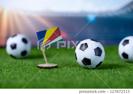 Seychelles flag with miniature soccer balls on green grass, set against a blurred stadium backdrop, symbolizing international football competition and national pride 127672515