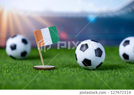 Ivory Coast national flag prominently displayed alongside miniature soccer balls on green grass, symbolizing international football competition and national pride Ivory Coast national flag prominently displayed alongside miniature soccer balls on green grass, symbolizing international football competition and national pride 127672519