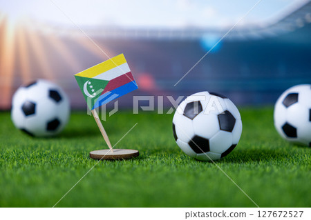Miniature Comoros flag stands on green grass with soccer balls, symbolizing national team pride, global sport, and international football championship 127672527