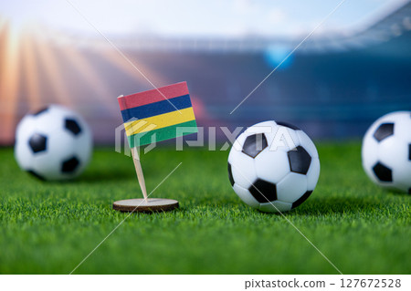 Miniature national flag of Mauritius with soccer balls on green grass, symbolizing global football competition and national team spirit in a stadium Miniature national flag of Mauritius with soccer balls on green grass, symbolizing global football competition and national team spirit in a stadium 127672528
