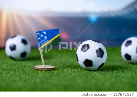 Miniature flag of Solomon Islands standing on artificial grass with classic soccer balls, set in a stadium, symbolizing global football competition and national pride Miniature flag of Solomon Islands standing on artificial grass with classic soccer balls, set in a stadium, symbolizing global football competition and national pride 127672537
