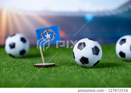 Miniature flag of Northern Mariana Islands with soccer balls on lush green grass field, representing international football tournaments and national team spirit Miniature flag of Northern Mariana Islands with soccer balls on lush green grass field, representing international football tournaments and national team spirit 127672538