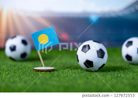 Miniature flag of Palau stands on green artificial grass with classic soccer balls, representing national pride and global football competition in a stadium setting Miniature flag of Palau stands on green artificial grass with classic soccer balls, representing national pride and global football competition in a stadium setting 127672553