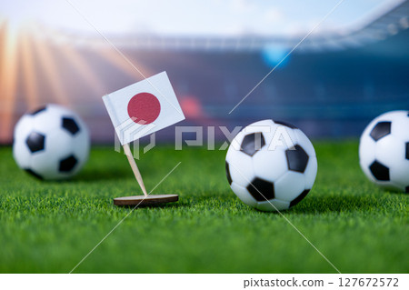 Miniature Japanese flag with soccer balls on a green field, representing national sports pride and international football competition in a stadium setting with copy space Miniature Japanese flag with soccer balls on a green field, representing national sports pride and international football competition in a stadium setting with copy space 127672572
