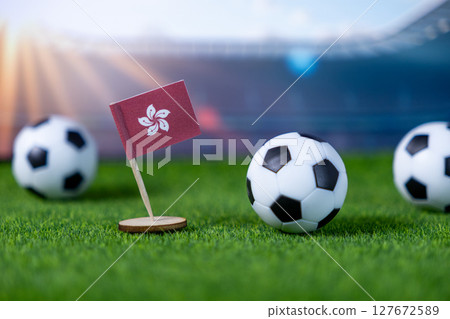 Miniature Hong Kong flag and classic soccer balls on vibrant green stadium grass, representing international football tournaments and national pride 127672589